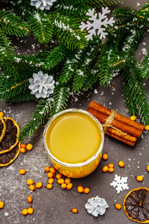 Festive low alcoholic fruit cocktail with fresh sea buckthorn berries, dry lemon slices and cinnamon sticks. Christmas or New Year sweet drink, evergreen fir branches. Black stone background, top viewの写真素材