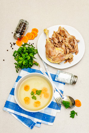 Transparent chicken broth with boiled meat. Low fat clear soup with carrot, parsley and spices. Hot dish, cutlery, stone concrete background, top viewの写真素材