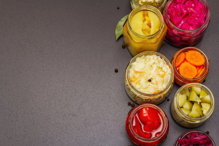 Assorted of fermented vegetables in glass jars. Preserved season vegetables concept, probiotics food for healthy lifestyle. Black stone concrete background, top viewの写真素材