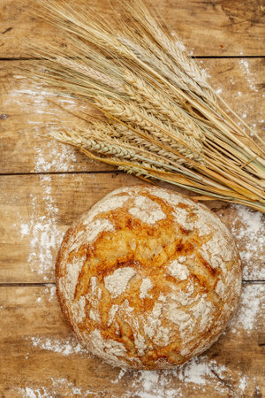 Fresh baked bread with wheat ears. Vintage wooden boards table, kneading the dough, top viewの写真素材