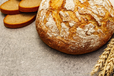 Fresh baked bread with wheat ears and vintage linen napkin. Gray stone concrete background, close up