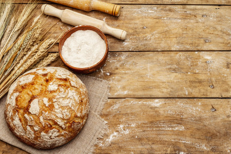 Fresh baked bread with wheat ears, bowl of flour and rolling pins. Vintage wooden boards table, kneading the dough, top viewの写真素材