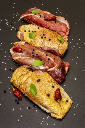 Raw duck breasts with sea salt, fresh basil, chili and spices. Poultry meat, natural BIO product, domestic fowl. Black stone concrete background, close upの写真素材