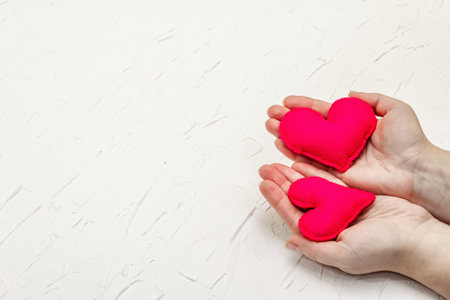 Valentine's Day concept. Female hands are holding a homemade felt hearts. White putty textured backgroundの写真素材