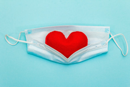 Red heart with medical protection mask on light blue background, top view, copy space. Concept of...