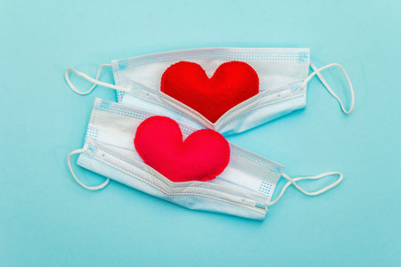 Red and pink hearts with medical protection masks on light blue background, top view, copy space. Concept of healthcare, self-defenseの写真素材