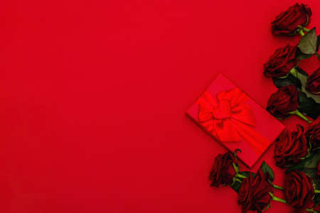 Bouquet of fresh burgundy roses and gift box on a matte red foamiran background. Fragrant red...
