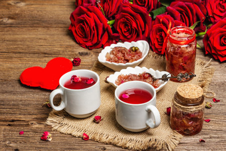 Tea time with rose petals jam and hot beverage. Homemade sweet breakfast, bouquet of fresh roses and assorted festive hearts. Valentines Day concept, old wooden tableの写真素材