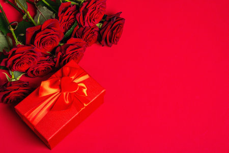 Bouquet of fresh burgundy roses and gift box on a matte red foamiran background. Fragrant red flowers, gift concept for Valentine's Day, Wedding or Birthdayの写真素材