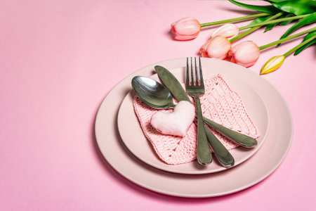 Romantic dinner table. Love concept for Valentine's or mother's day, wedding cutlery. Minimalistic style, rose plates, a bouquet of tulip, crochet napkin, place for textの写真素材