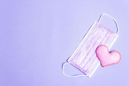 Lilac heart with medical protection mask on light purple background. Concept of healthcare, self-defenseの写真素材