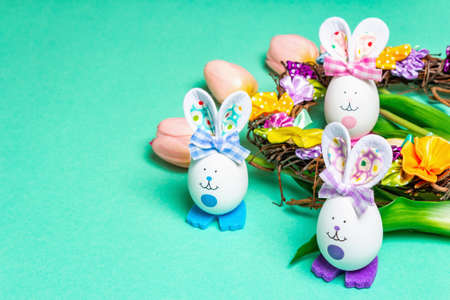 Traditional Easter symbols concept. Cute rabbits from eggs, wicker wreath with flowers, gentle tulips. Pastel turquoise backgroundの写真素材