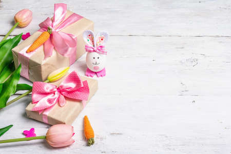 Handmade traditional Easter symbols concept. Cute rabbit from the egg, gift box, festive decor in pink tones. White wooden background, copy spaceの写真素材