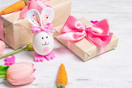 Handmade traditional Easter symbols concept. Cute rabbit from the egg, gift box, festive decor in...