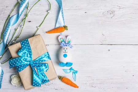 Handmade traditional Easter symbols concept. Cute rabbit from the egg, gift box, festive decor in blue tones. White wooden background, top viewの写真素材