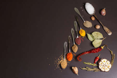 Assorted spices in spoons, dry herbs and vegetables on black stone background. Healthy food preparation concept, place for textの写真素材