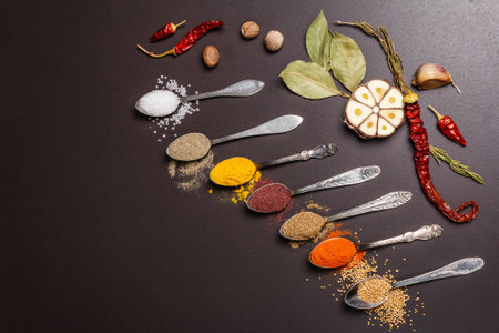 Assorted spices in spoons, dry herbs and vegetables on black stone background. Healthy food preparation concept, place for textの写真素材