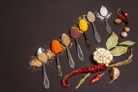 Assorted spices in spoons, dry herbs and vegetables on black stone background. Healthy food preparation concept, place for textの写真素材