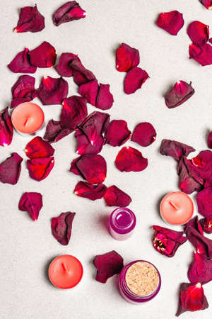 Floral and spa concept with dried roses petals, fragrant candles and soft towel. Natural rose oil, light stone concrete background, top viewの写真素材