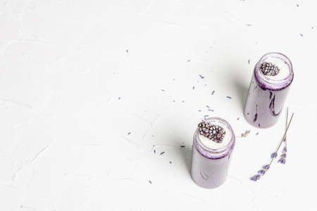 Lavender smoothie with coconut flakes and frozen blackberry. Dry flower bouquet, lilac napkin. White putty background, top viewの写真素材
