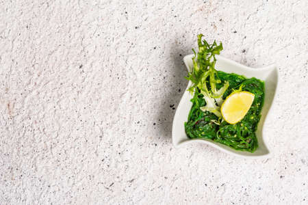 Traditional Asian chukka salad with peanut sauce in a bowl. Meal decorated lemon wedge and herbs. Healthy food concept, light colors stone background, top viewの写真素材