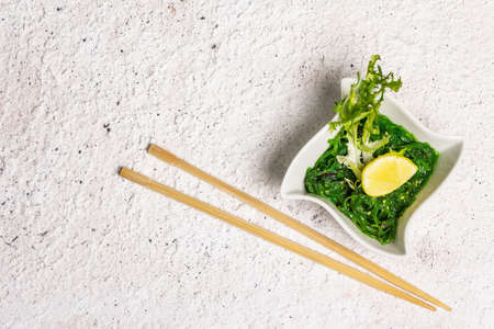 Traditional Asian chukka salad with peanut sauce in a bowl. Meal decorated lemon wedge and herbs. Healthy food concept, light colors stone background, top viewの写真素材