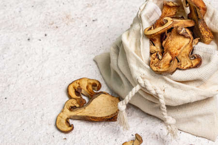 Forest dried edible mushrooms in a linen sack. Dehydrated slices, exquisite ingredient for cooking healthy food. Light colors plaster background, top viewの写真素材
