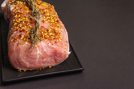 Raw pork loin. Fresh meat with rosemary and flakes spices on the ceramic stand. Black stone concrete backgroundの写真素材