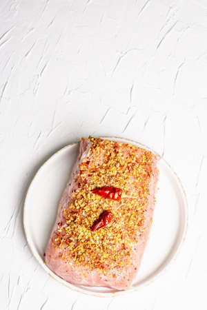 Raw organic meat. Pork fillet for grilling, baking or frying. Flakes spices, ceramic plate on white putty background, top viewの写真素材