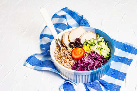 Buddha Bowl. Buckwheat, baked lean pork, red cabbage, cucumber, tomato, olives, flax seeds. Healthy food concept, white putty background, place for textの写真素材
