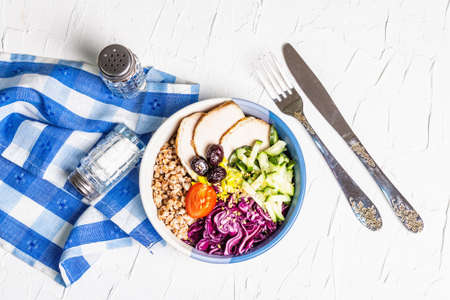 Buddha Bowl. Buckwheat, baked lean pork, red cabbage, cucumber, tomato, olives, flax seeds. Healthy food concept, white putty background, top viewの写真素材