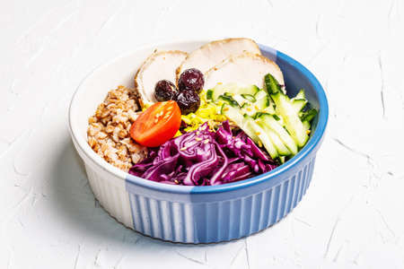 Buddha Bowl. Buckwheat, baked lean pork, red cabbage, cucumber, tomato, olives, flax seeds. Healthy food concept, white putty background, place for textの写真素材
