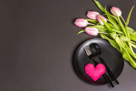 Festive creative black table setting with tulips and felt heart on dark background. Valentine's Day, Wedding, Birthday, Women's, and Mother's Day. Flat lay, top viewの写真素材