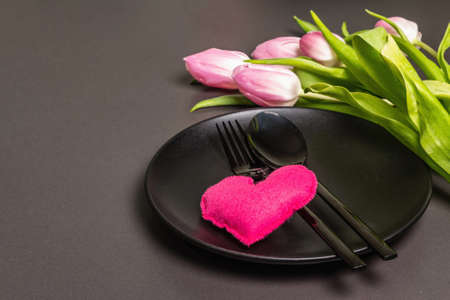 Festive creative black table setting with tulips and felt heart on dark background. Valentine's Day,...
