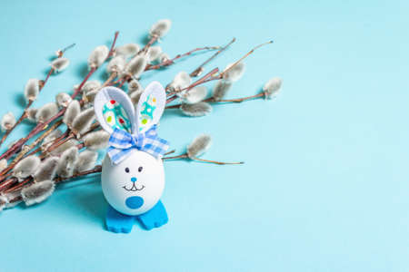 Sprig of willow isolated on pastel blue background. Willow seals, fluffy buds, handmade funny bunny from the egg. Happy Easter conceptの写真素材