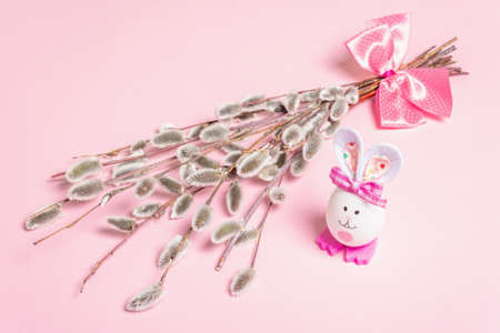 Sprig of willow isolated on pastel pink background. Willow seals, fluffy buds, handmade funny bunny from the egg. Happy Easter conceptの写真素材