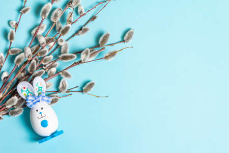 Sprig of willow isolated on pastel blue background. Willow seals, fluffy buds, handmade funny bunny from the egg. Happy Easter conceptの写真素材