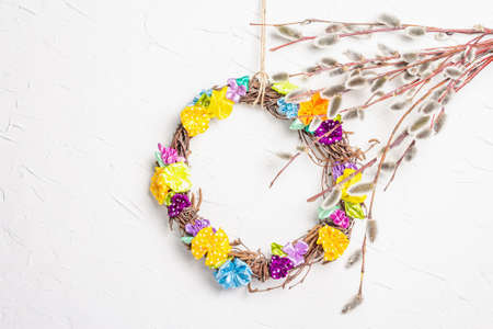 Sprig of willow and braided wreath on white putty texture wall. Willow seals, fluffy buds, handmade flowers. Happy Easter conceptの写真素材