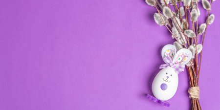 Sprig of willow isolated on pastel lilac background. Willow seals, fluffy buds, handmade funny bunny from the egg. Happy Easter concept, Bannerの写真素材