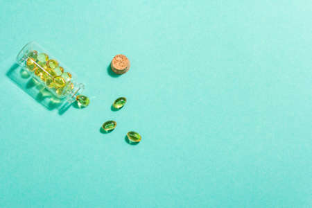 Omega-3 tablets in an old bottle on a turquoise matte background. Healthy life concept, prevention of various diseases. Trendy hard light, dark shadow, flat lay, mockup, template, top viewの写真素材