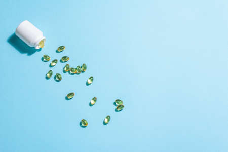 Omega-3 tablets scattered from the bottle on a blue matte background. Healthy life concept, prevention of various diseases. Trendy hard light, dark shadow, flat lay, mockup, template, top viewの写真素材