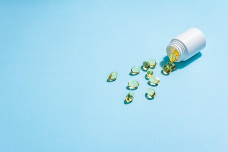 Omega-3 tablets scattered from the bottle on a blue matte background. Healthy life concept,...
