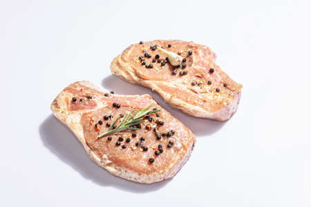 Two raw pork loin steaks isolated on white background. Fresh garlic, fragrant rosemary, black peppercorn, sea salt. A modern hard light, dark shadow, flat lay, mockup, templateの写真素材