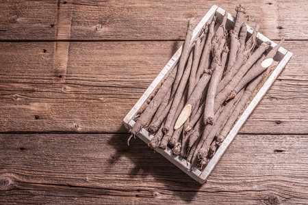 Raw Scorzonera or Spanish salsify in a crate. Modern vegetables, healthy food, suitable for diabetics. A trendy hard light, dark shadow, wooden table, top viewの写真素材