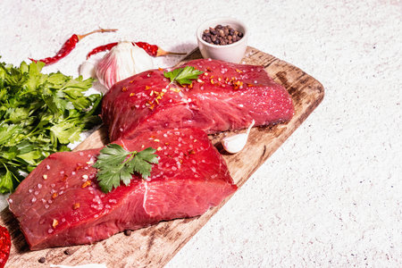 Raw beef steaks on a wooden cutting board. Trendy hard light, dark shadow. Spices, hot chili, fresh...