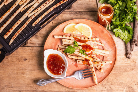 Grilled scorzonera with sauce. Cutlery, rustic ceramic plates, grill, spices. Old wooden boards...