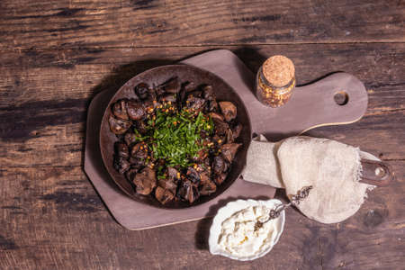 Fried royal champignons in an old cast-iron skillet. Trendy hard light, dark shadow. Vintage wooden table, rustic food style concept, top viewの写真素材