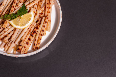 Grilled scorzonera, trendy vegan food. Modern hard light, dark shadow. Ceramic stand, lemon,...