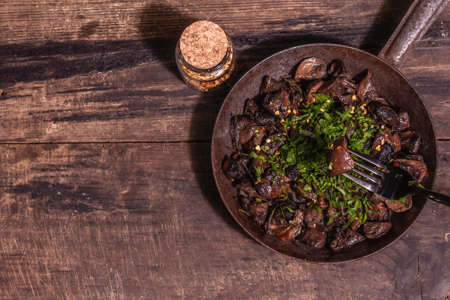 Fried royal champignons in an old cast-iron skillet. Trendy hard light, dark shadow. Vintage wooden table, rustic food style concept, top viewの写真素材