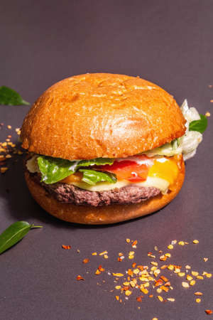 Fresh burgers, American fast food. Modern hard light, dark shadow. Scattered spices, fresh leaves, black stone concrete background, place for textの写真素材